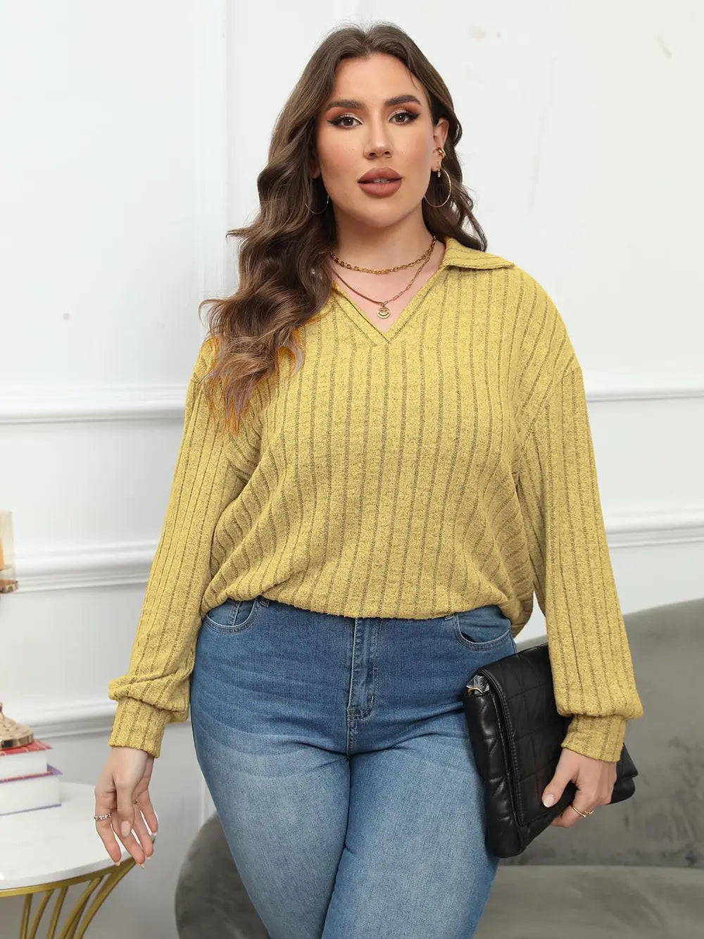 Woman wearing a yellow ribbed sweater and blue jeans, standing indoors.