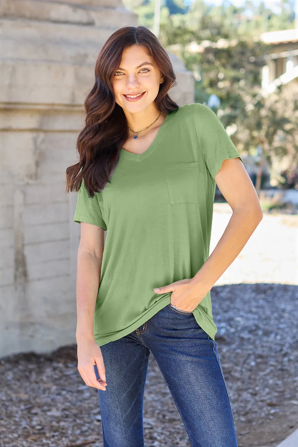 Woman wearing a green t-shirt with a pocket and blue jeans outdoors.