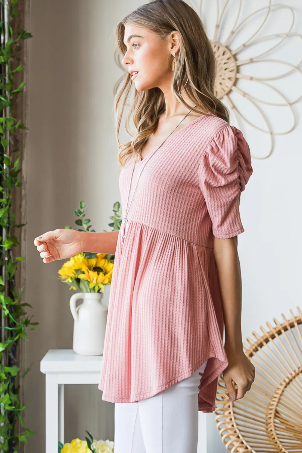 Woman wearing a pink blouse standing in a room with decorative elements.