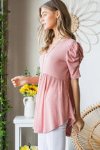 Woman wearing a pink blouse standing in a room with decorative elements.