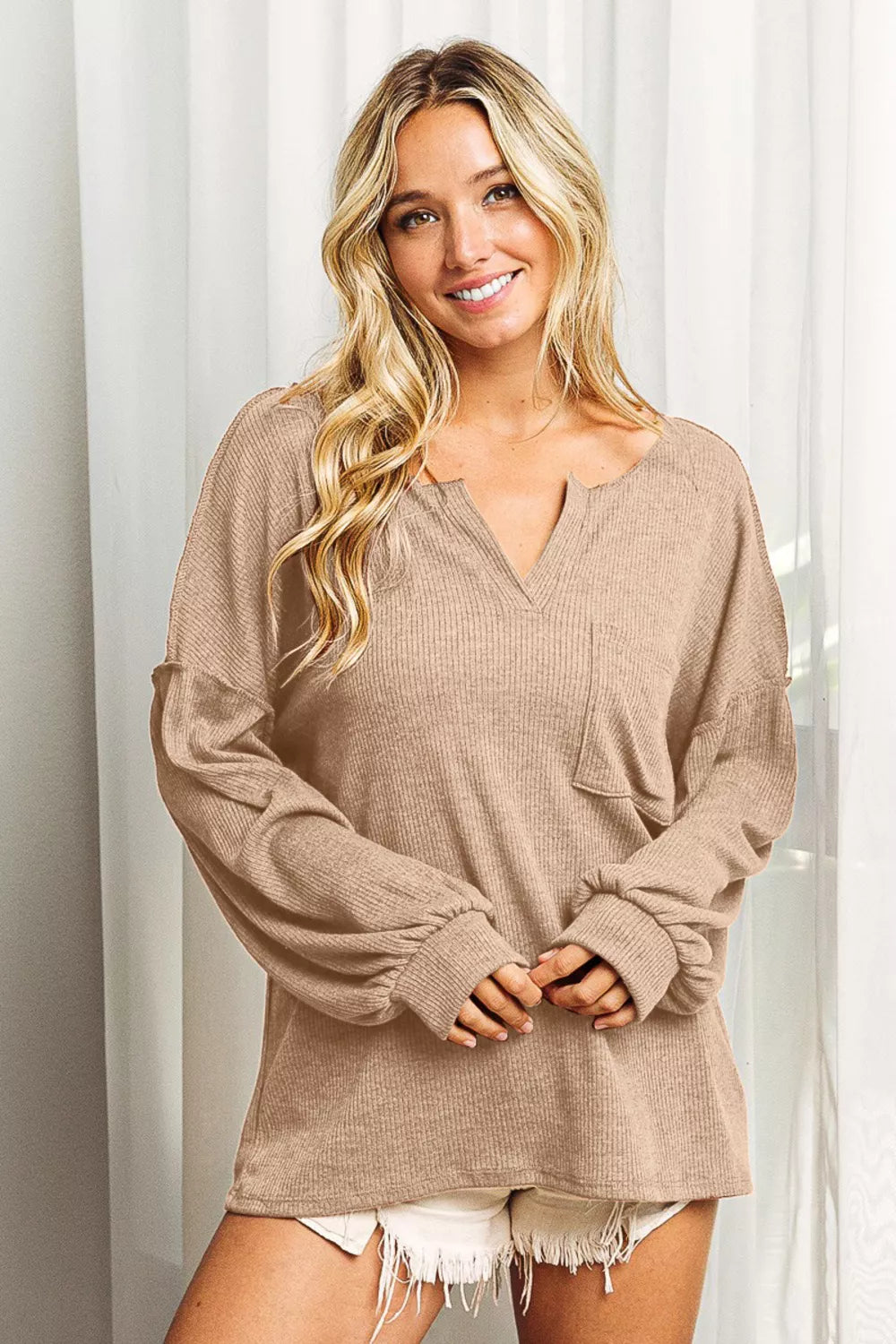 Woman wearing a beige long-sleeve top with a neutral background