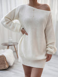 Person wearing a white off-shoulder sweater dress in a minimalistic room.