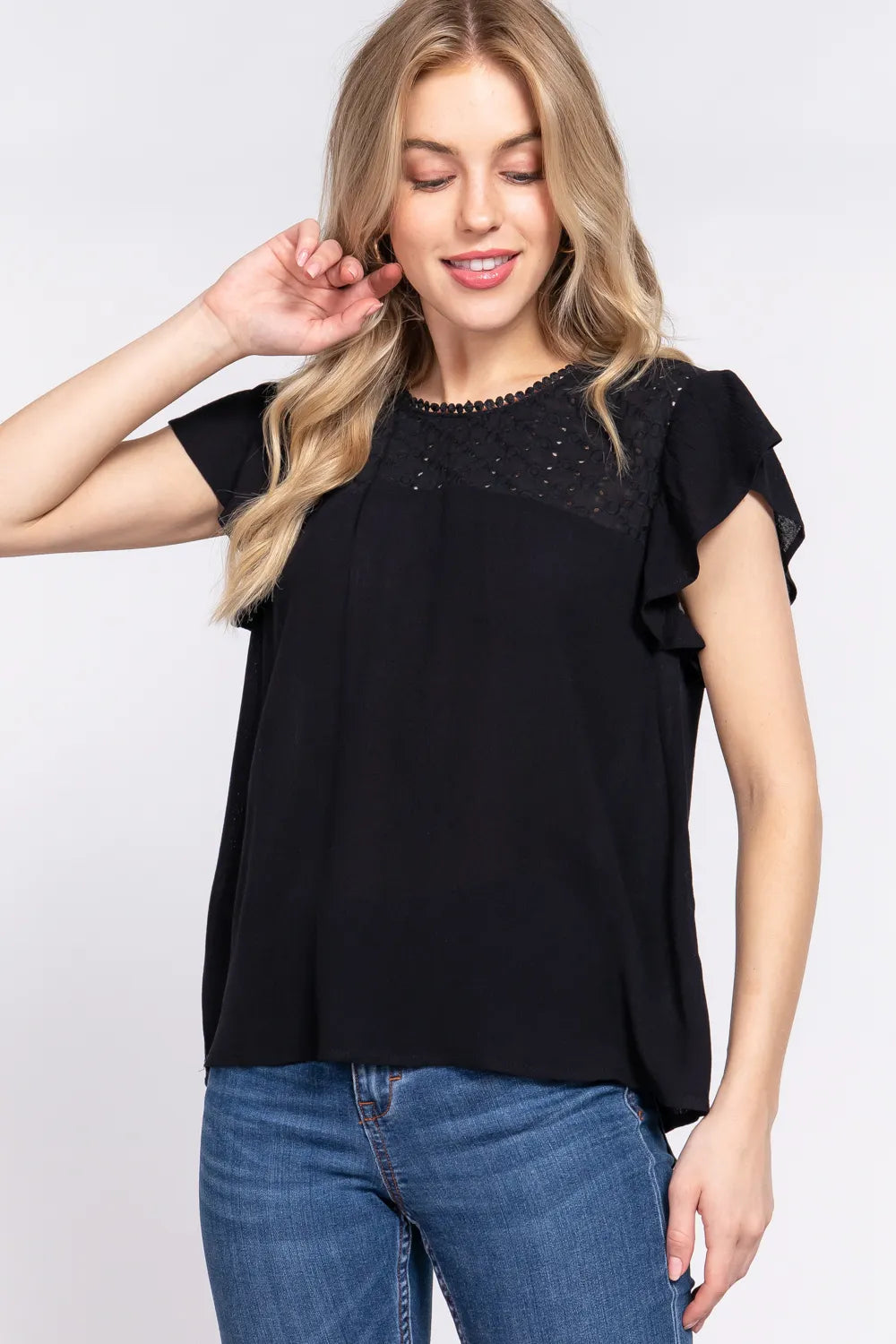 Woman wearing a black top with lace details and blue jeans on a white background