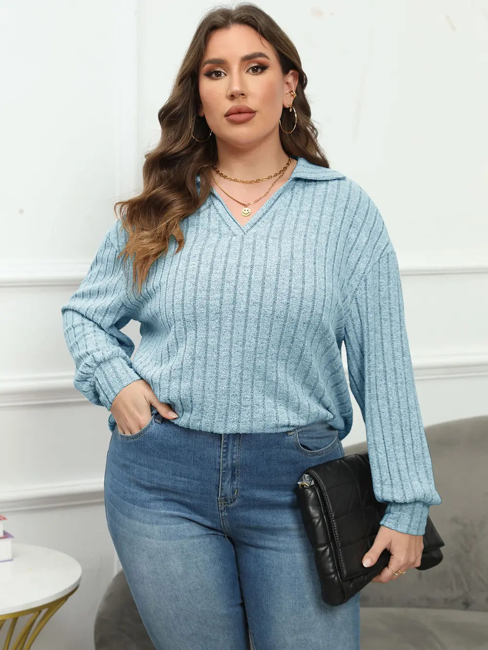 Woman wearing a light blue ribbed sweater and jeans, holding a black clutch.