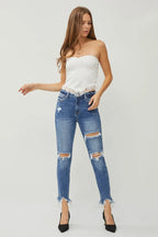 Woman wearing a white strapless top and blue ripped jeans on a light gray background