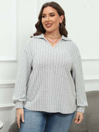 Woman wearing a light gray ribbed sweater with a hood and blue jeans against a white wall.