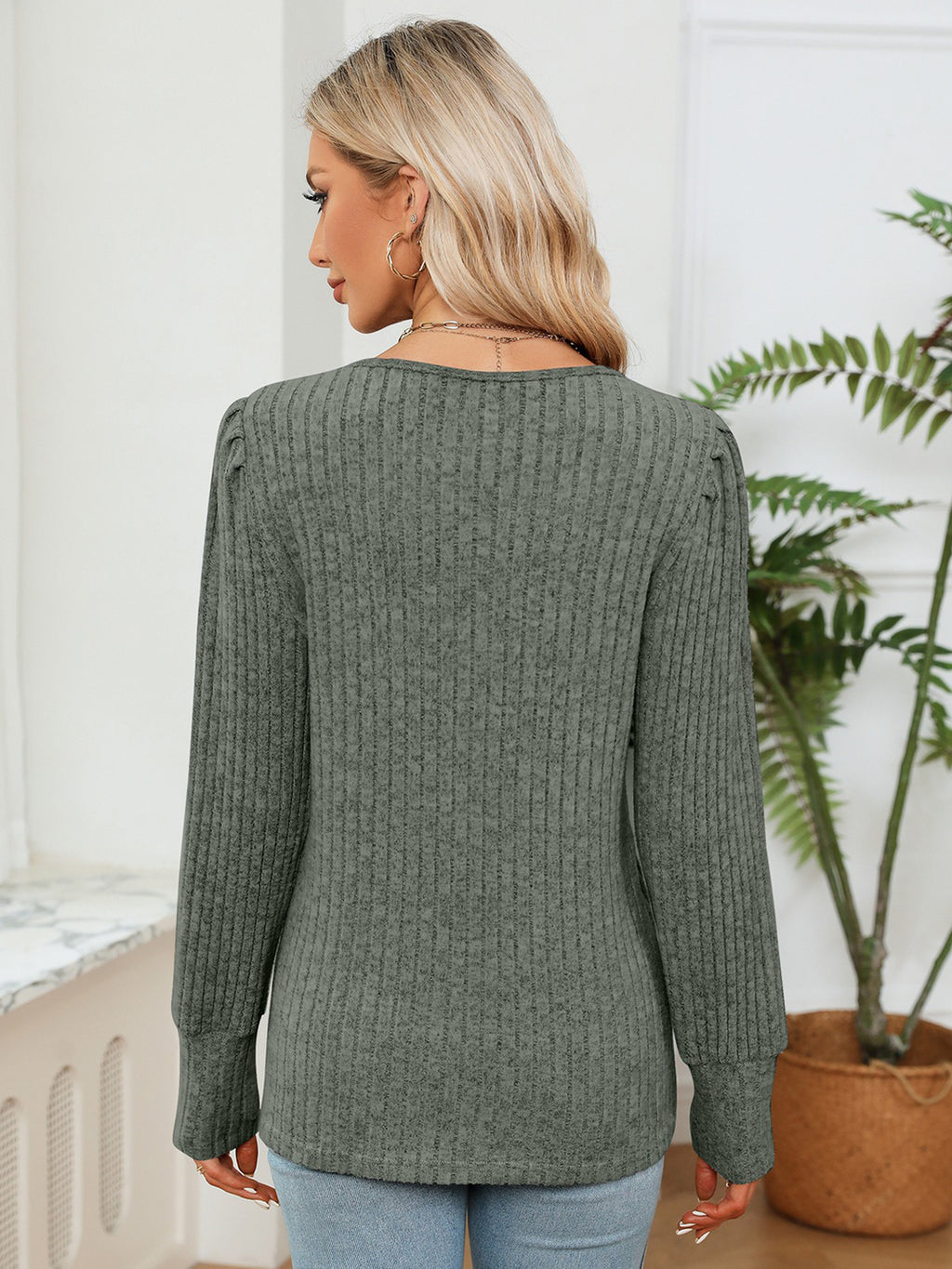 Woman wearing a green sweater in a room with a plant
