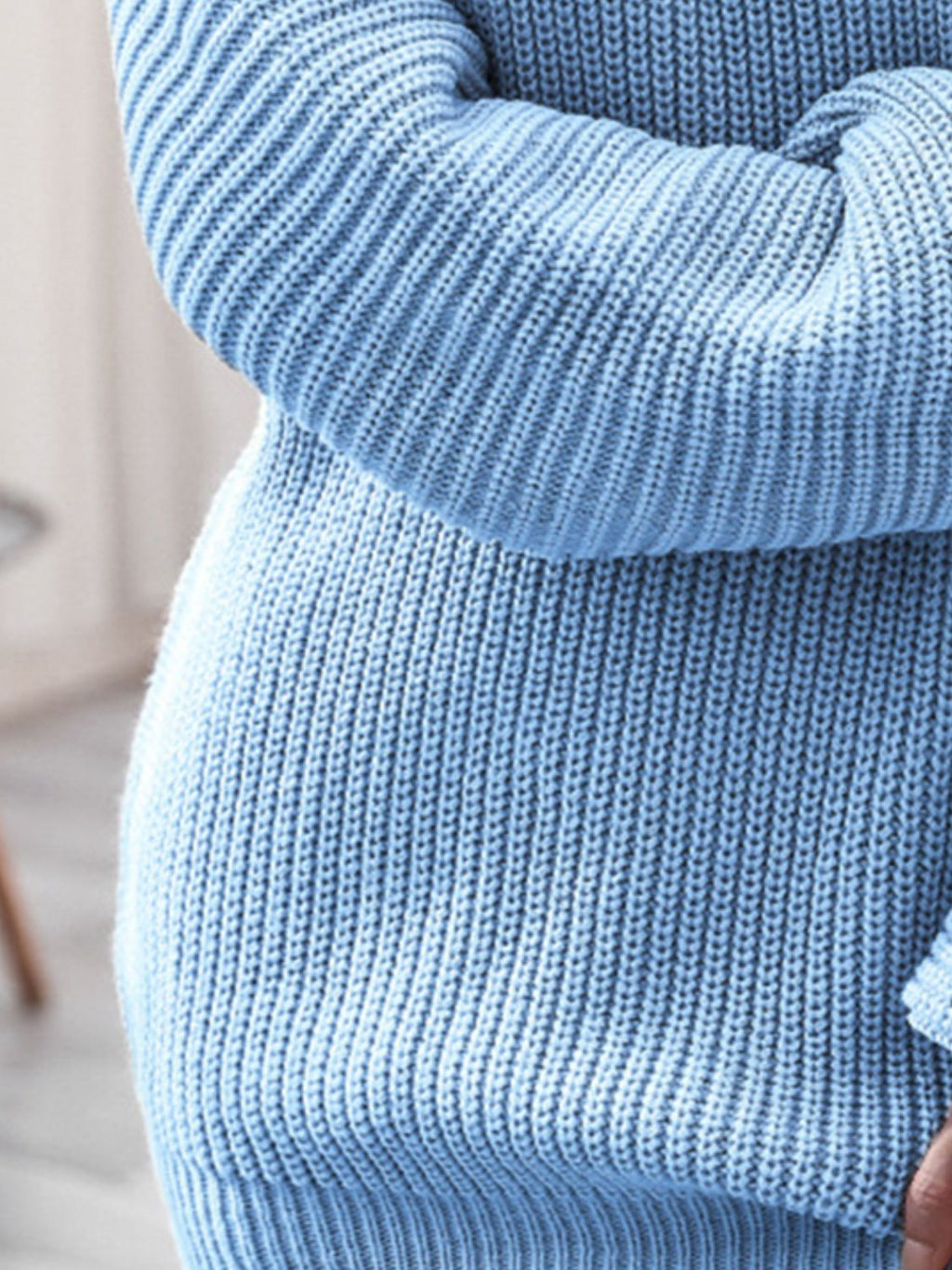 Close-up of a person wearing a light blue knitted sweater with a blurred background.