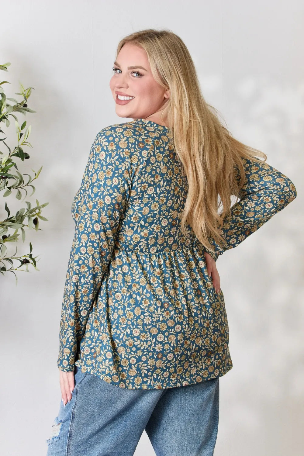 Woman wearing a floral blouse and jeans against a white background