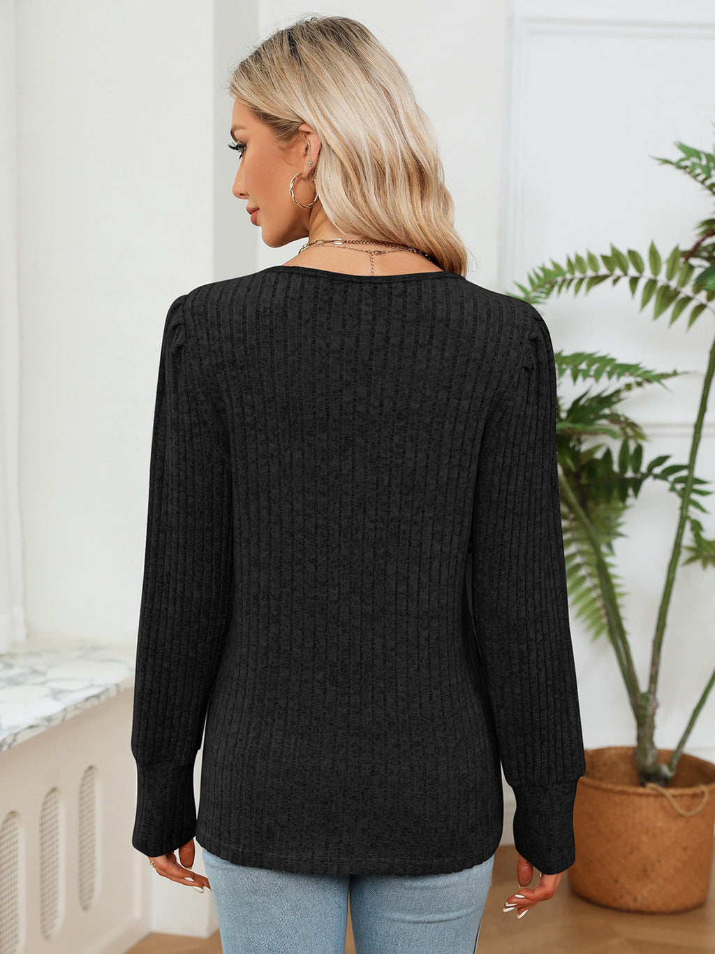 Woman wearing a black sweater in a room with a plant