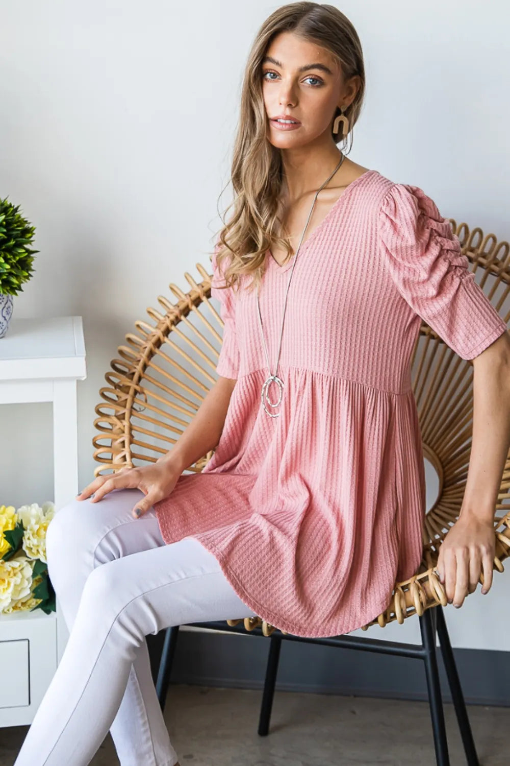 Woman wearing a pink dress sitting on a wicker chair indoors.