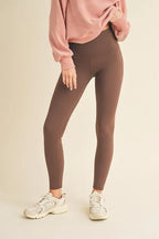 Person wearing gray leggings and a pink sweatshirt on a beige background