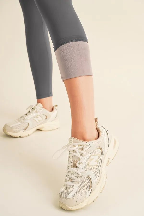 Person wearing light-colored sneakers and gray leggings on a neutral background