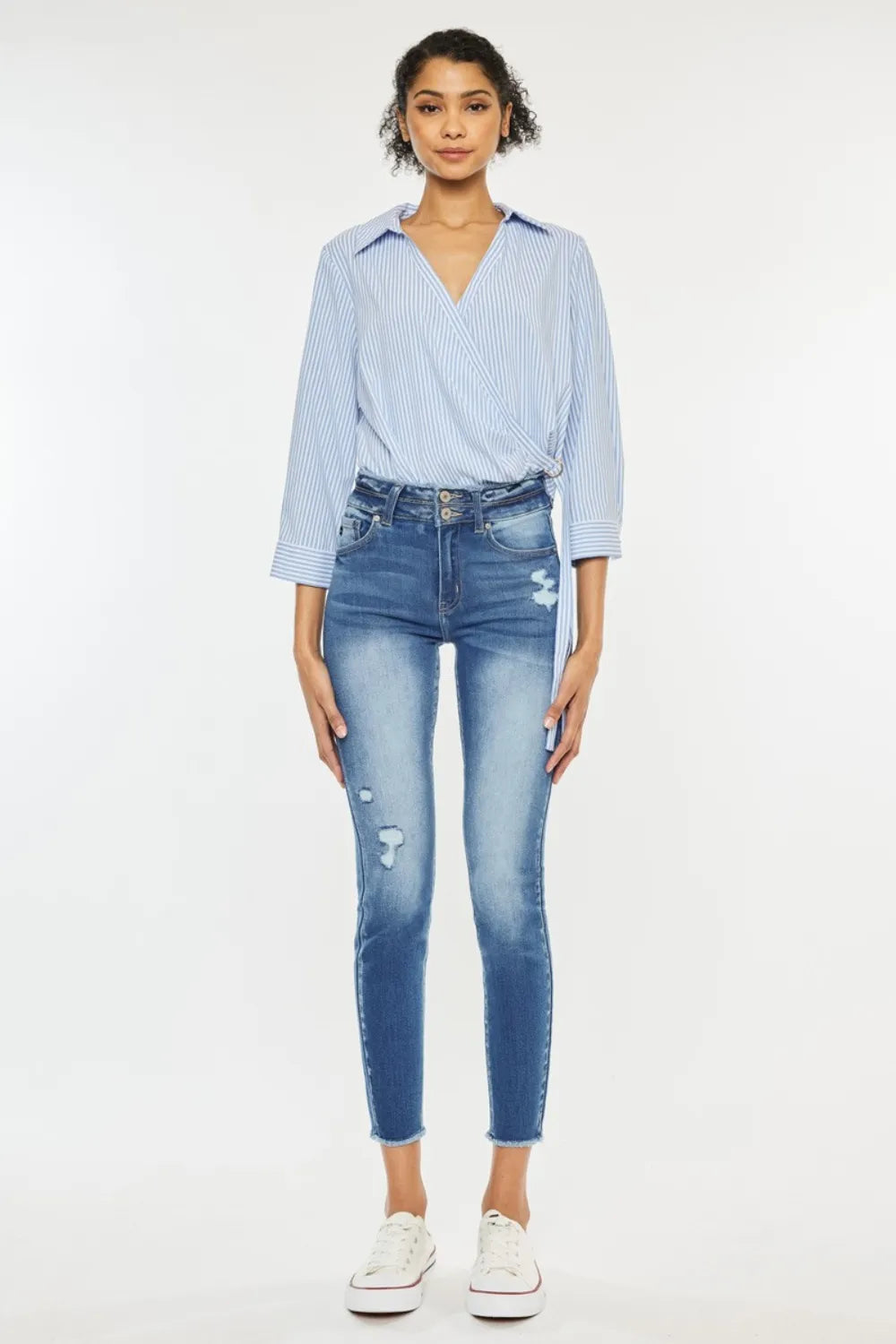 Woman wearing a light blue striped shirt and distressed jeans on a white background