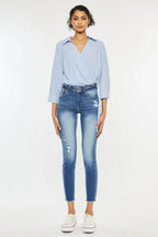 Woman wearing a light blue striped shirt and distressed jeans on a white background