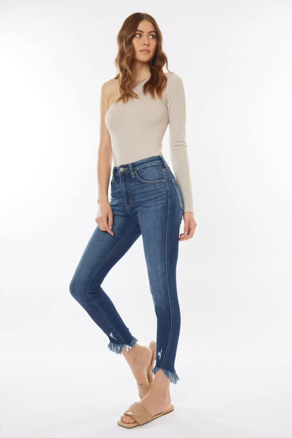 Woman wearing a beige long-sleeve top and blue jeans on a white background