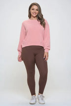Woman wearing a pink sweatshirt and brown leggings on a white background