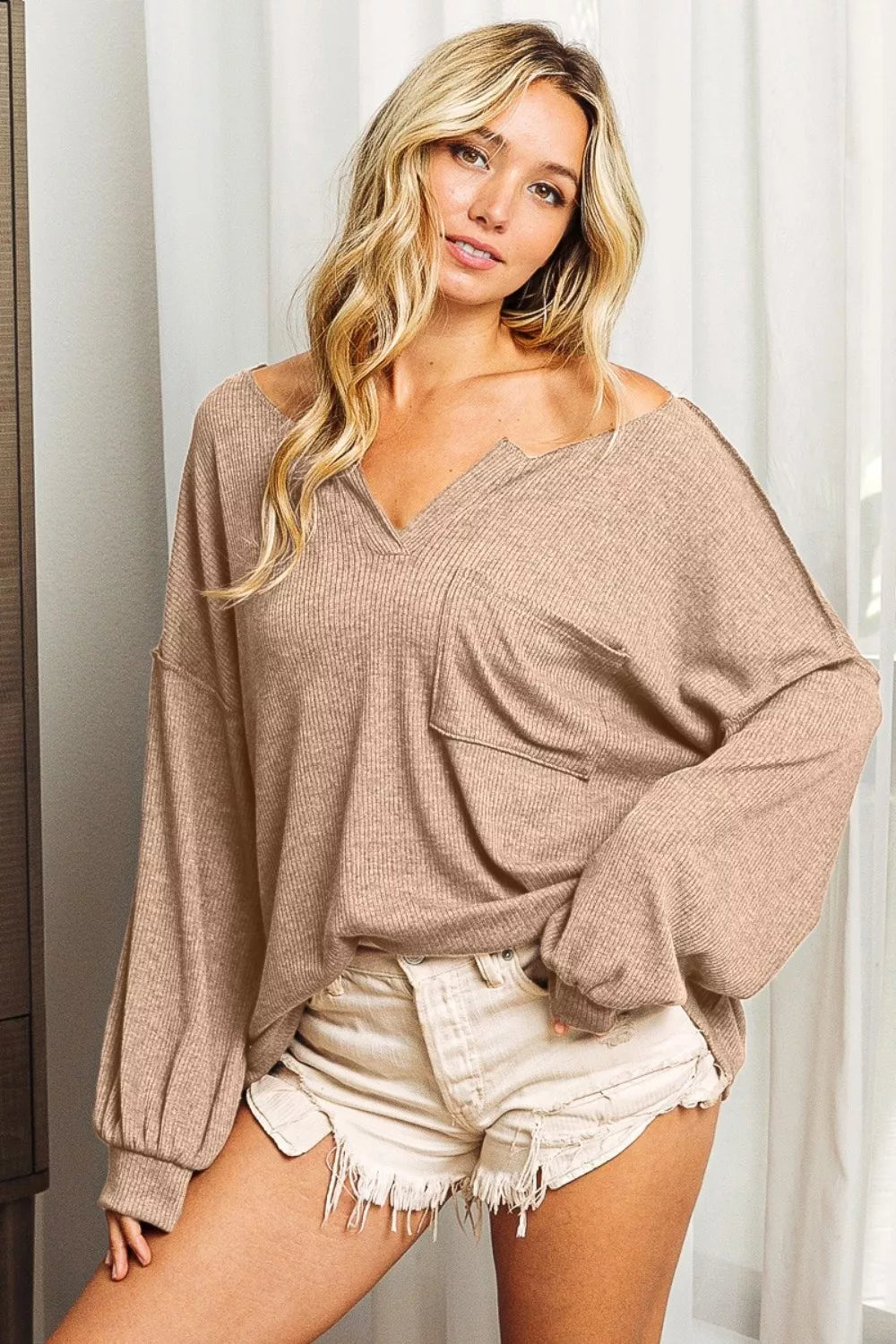 Woman wearing a beige oversized sweater and white shorts indoors.
