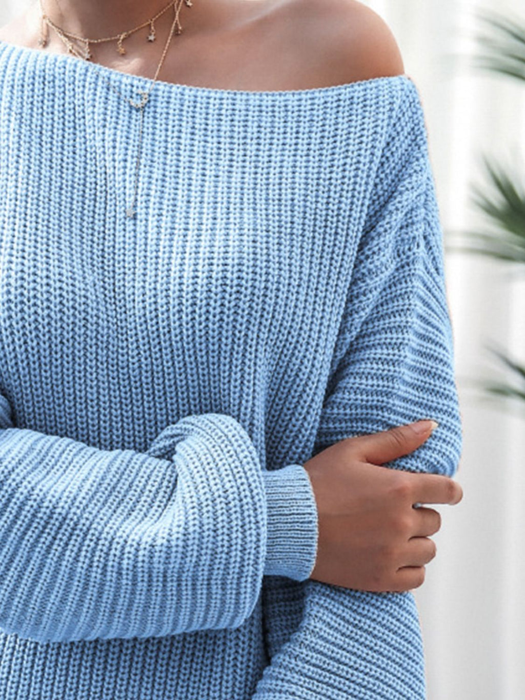 Close-up of a person wearing a blue off-shoulder sweater with blurred background