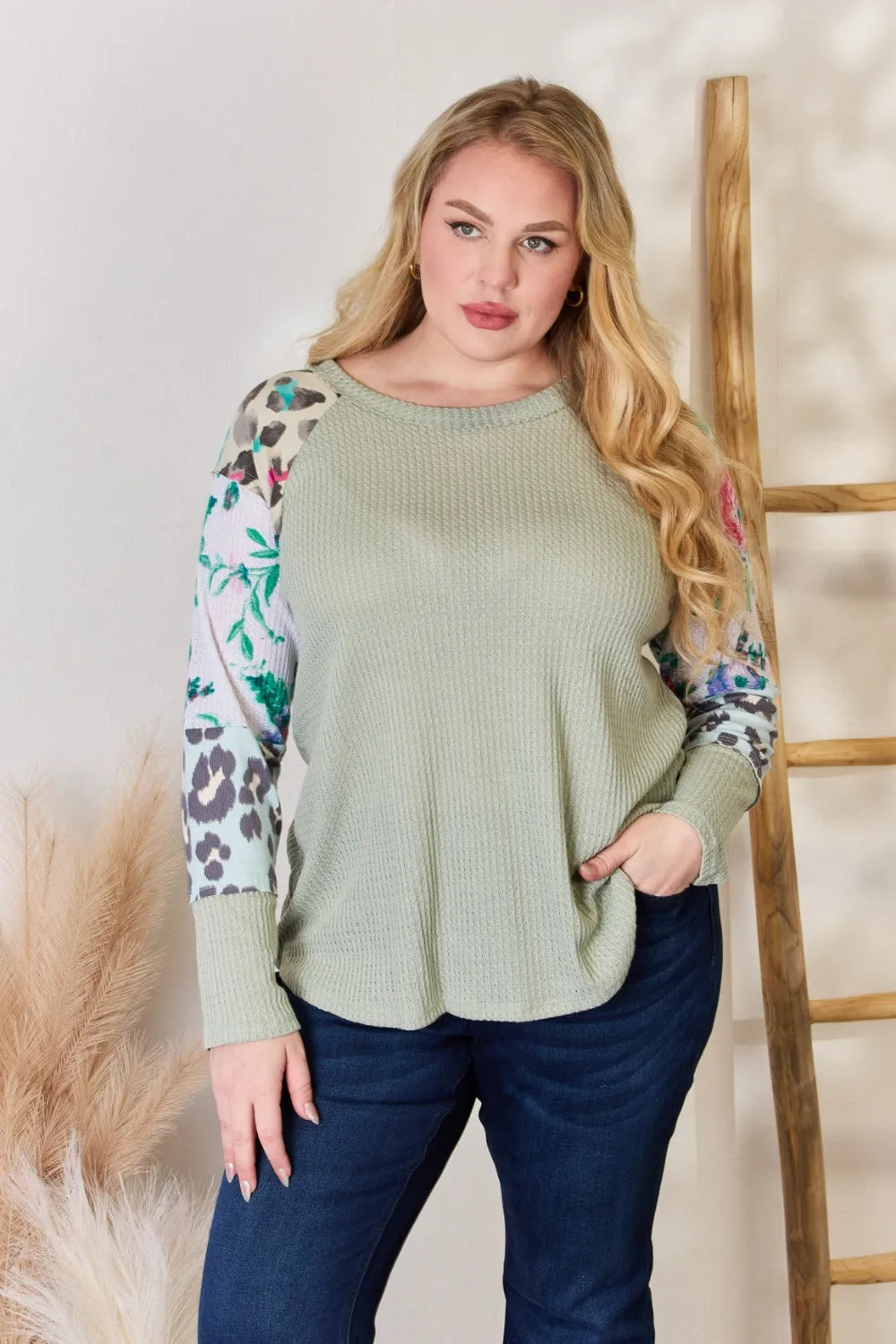 Woman wearing a green sweater with floral and leopard print sleeves against a neutral background