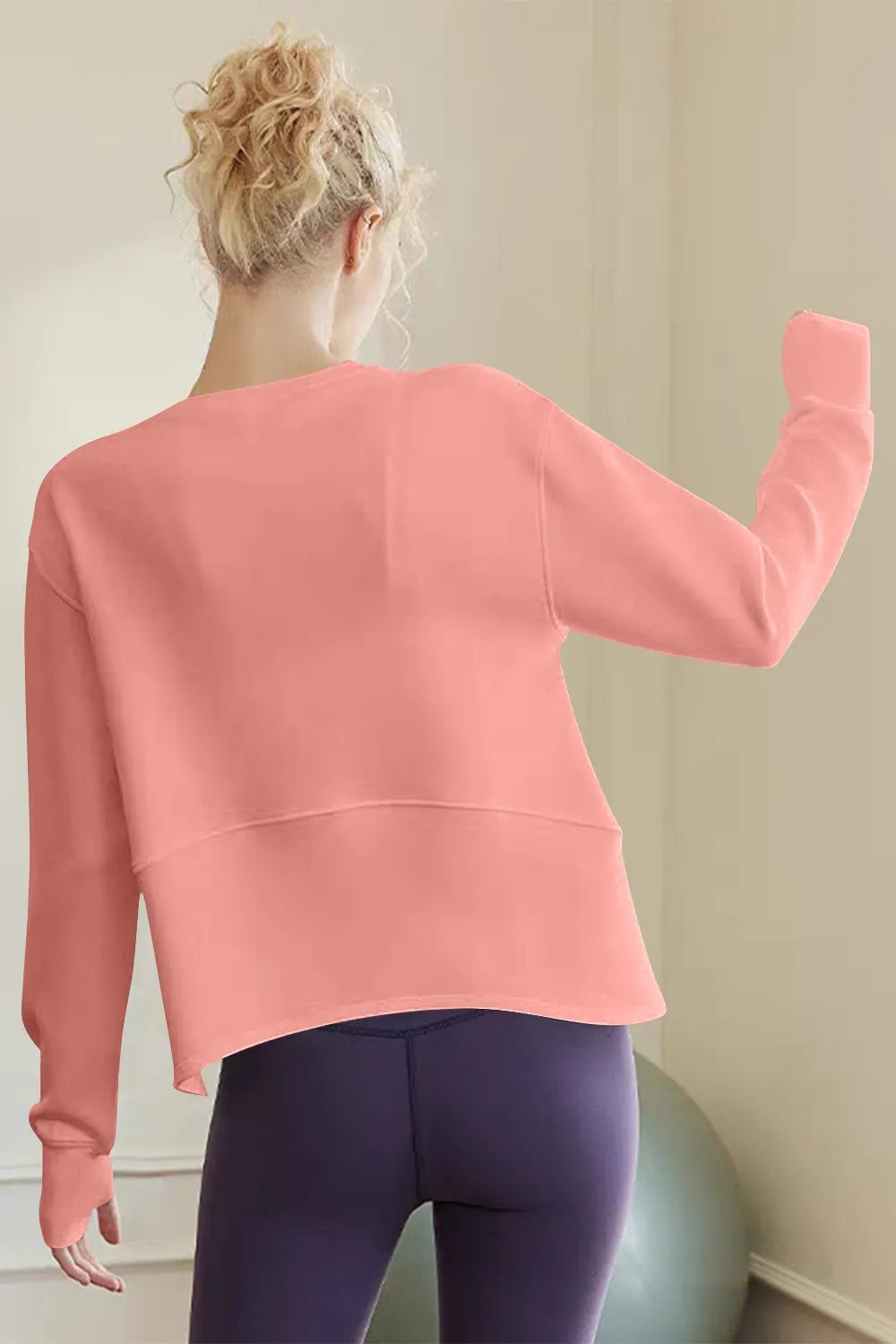 Person wearing a pink sweatshirt and purple leggings in a minimal indoor setting