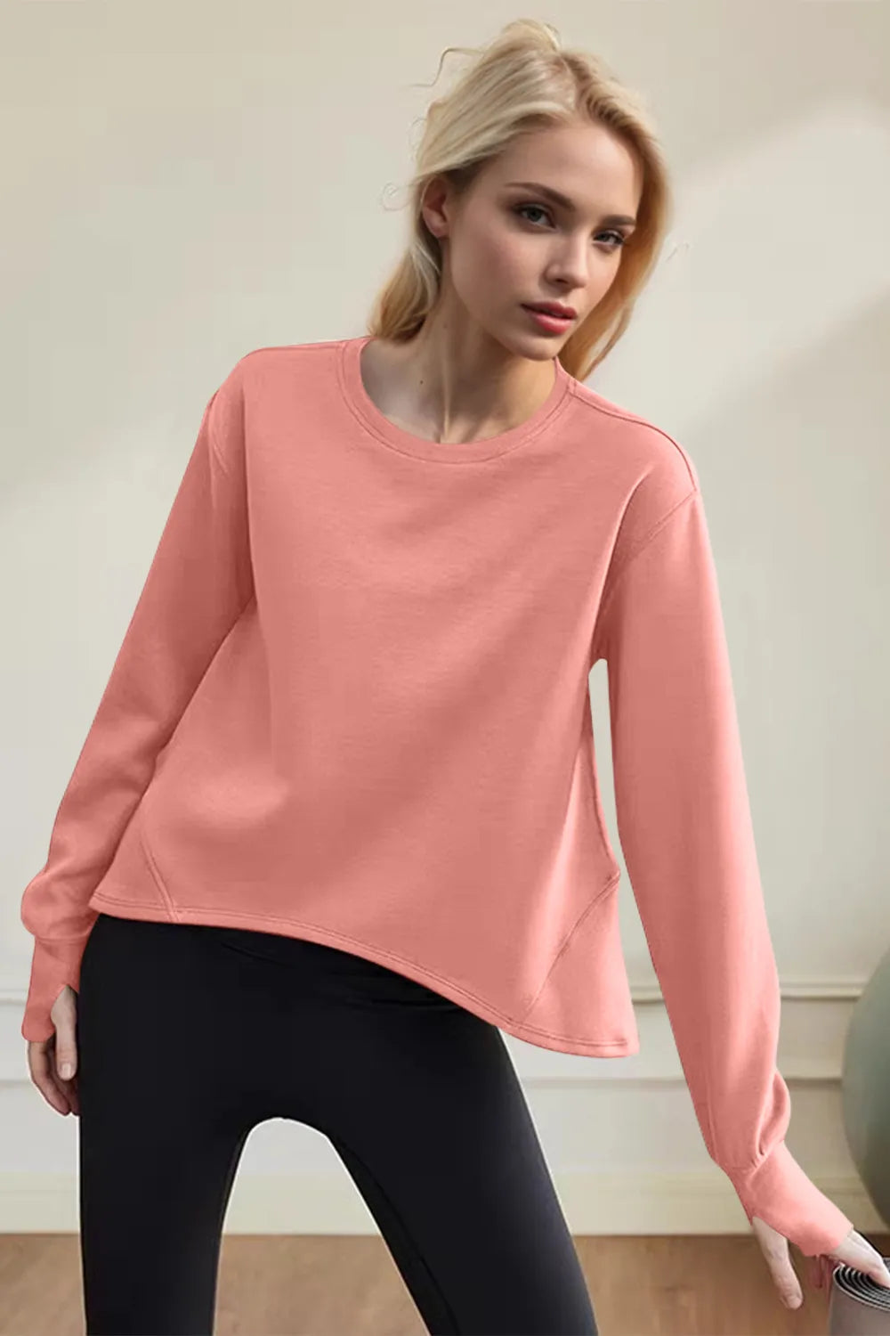 Woman wearing a pink sweatshirt and black leggings against a neutral background