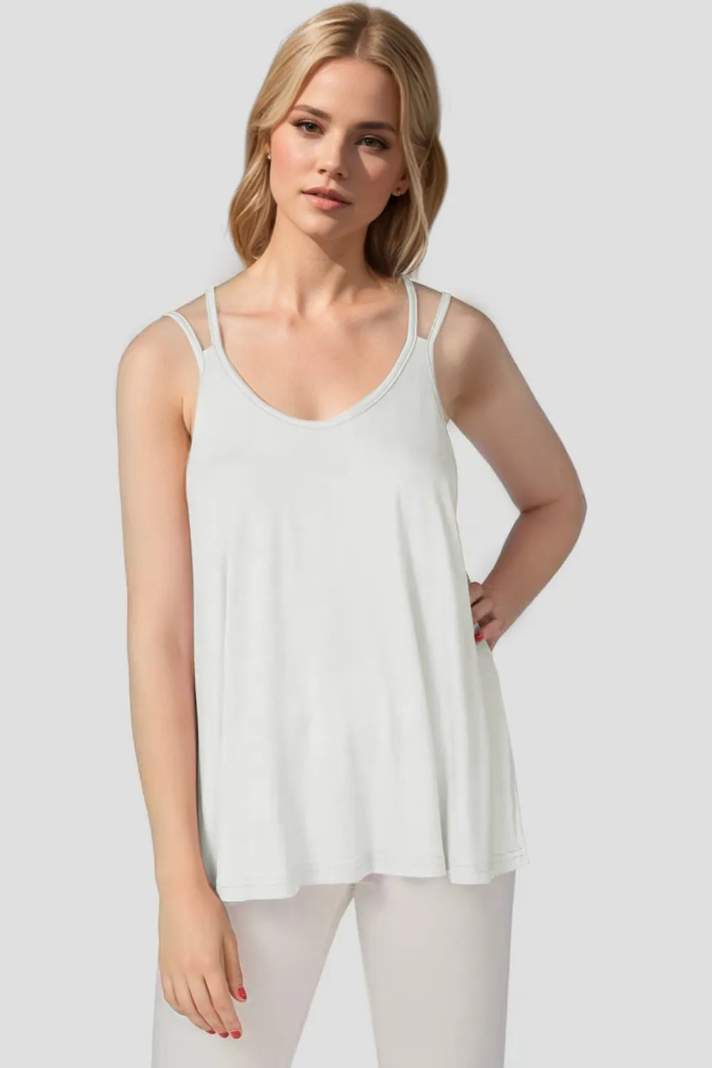 Woman wearing a white sleeveless top against a plain background