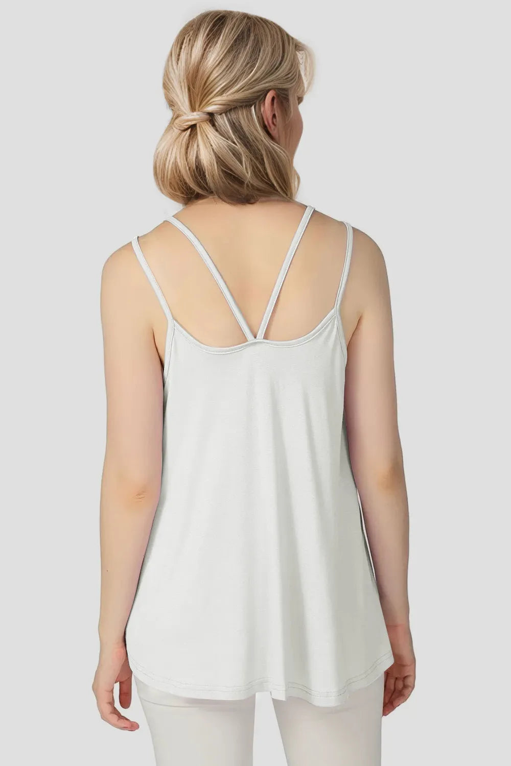 Woman wearing a white spaghetti strap top against a plain background
