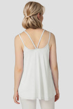 Woman wearing a white spaghetti strap top against a plain background