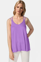 Woman wearing a purple tank top and white pants on a light gray background