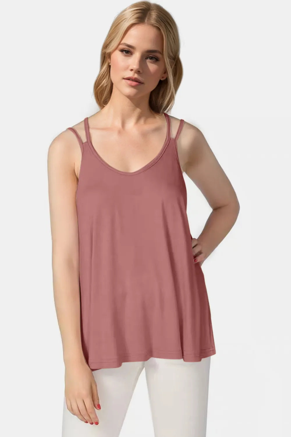 Woman wearing a mauve tank top and white pants on a light gray background