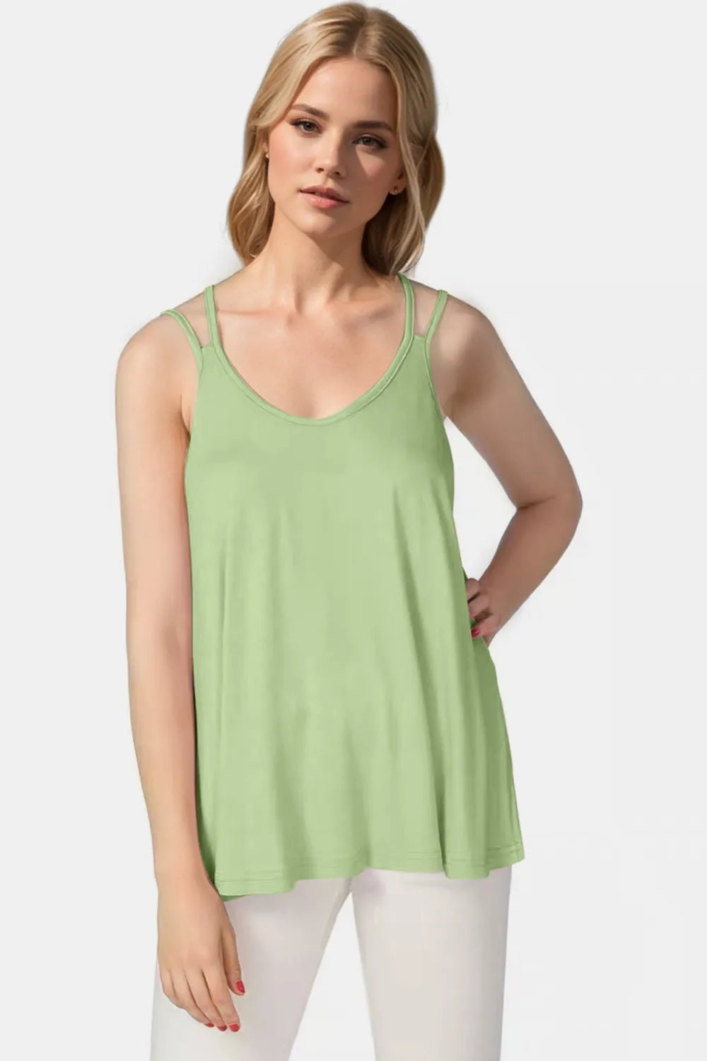 Woman wearing a light green tank top and white pants on a plain background
