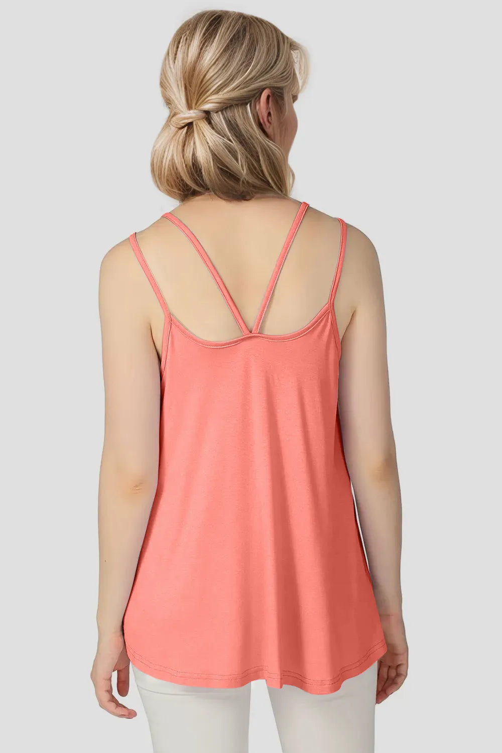Woman wearing a coral tank top with thin straps on a plain background