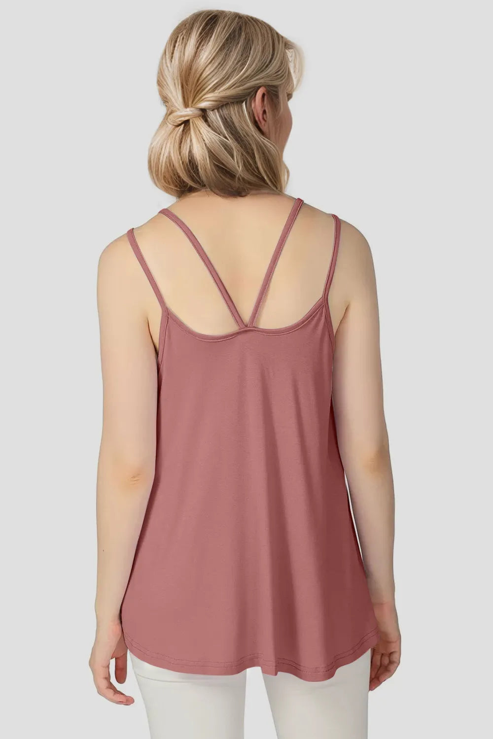 Woman wearing a pink tank top with thin straps on a plain background