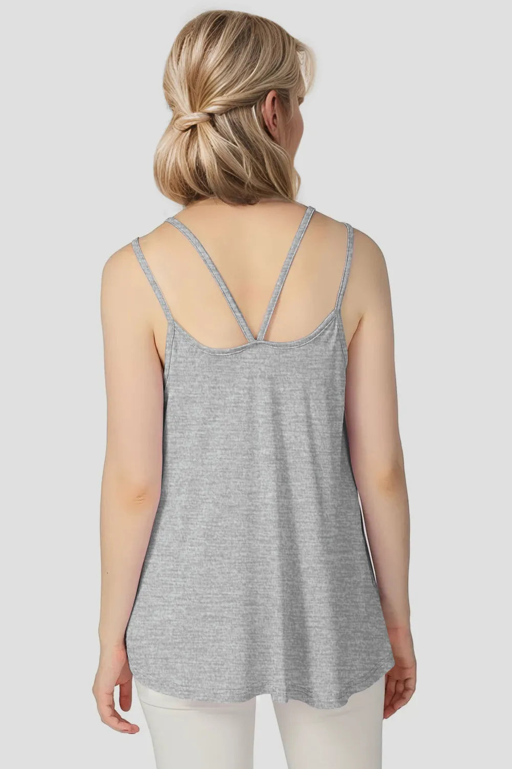 Woman wearing a gray tank top with thin straps on a plain background
