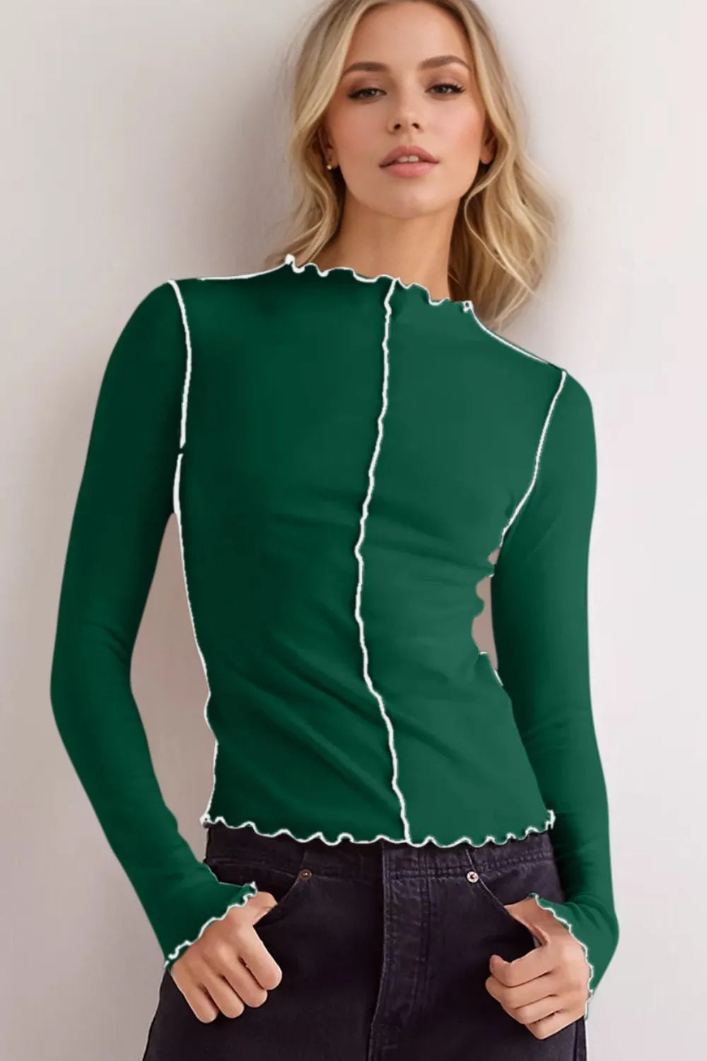 Woman wearing a green long-sleeve top with white trim against a plain background