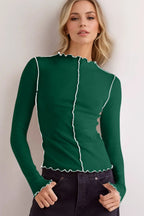 Woman wearing a green long-sleeve top with white trim against a plain background