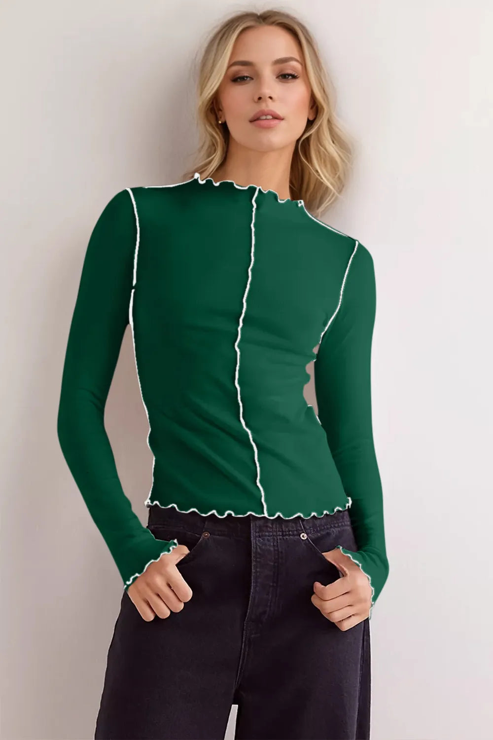 Woman wearing a green long-sleeve top with white trim against a plain background