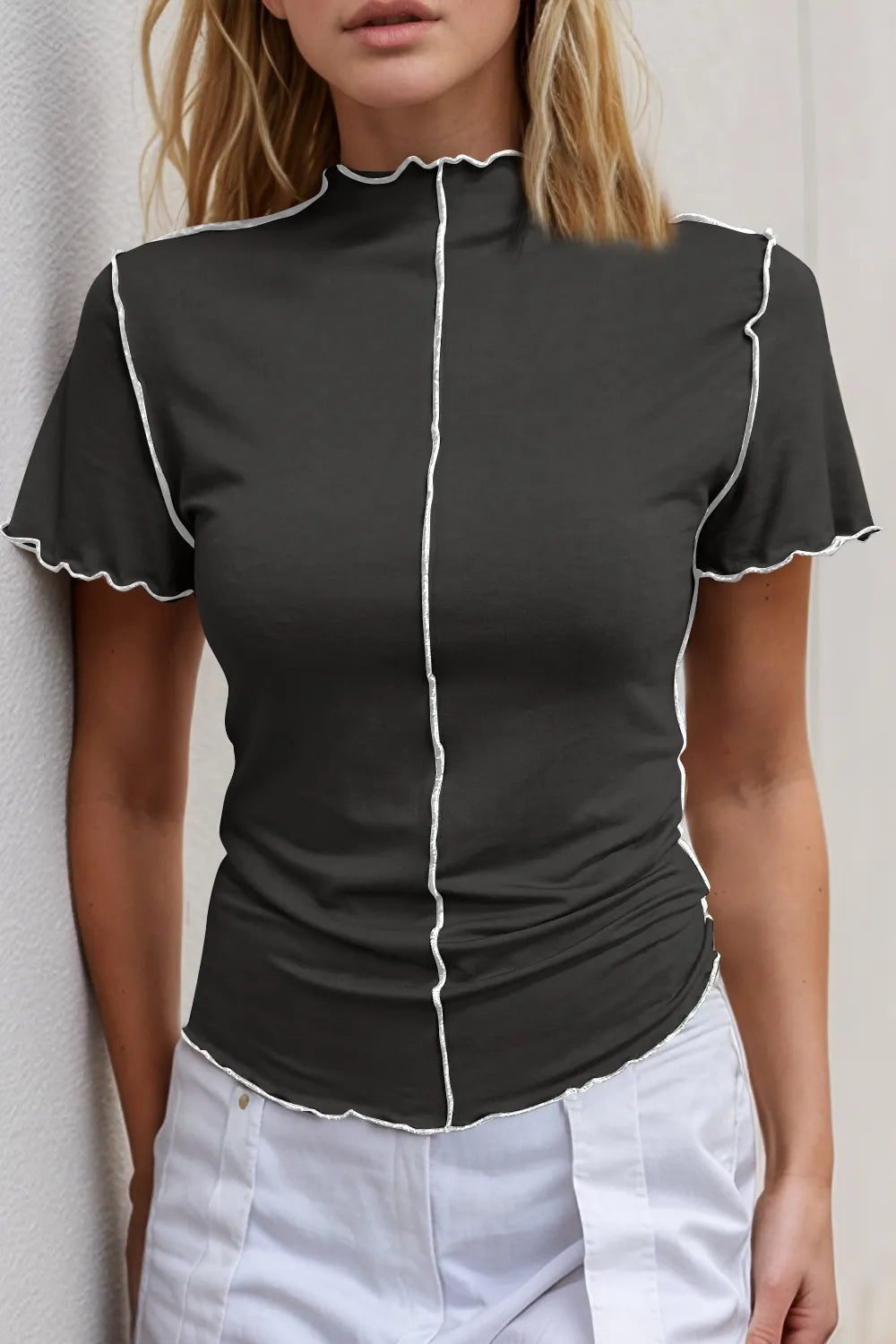Woman wearing a black short-sleeve top with white trim against a neutral background