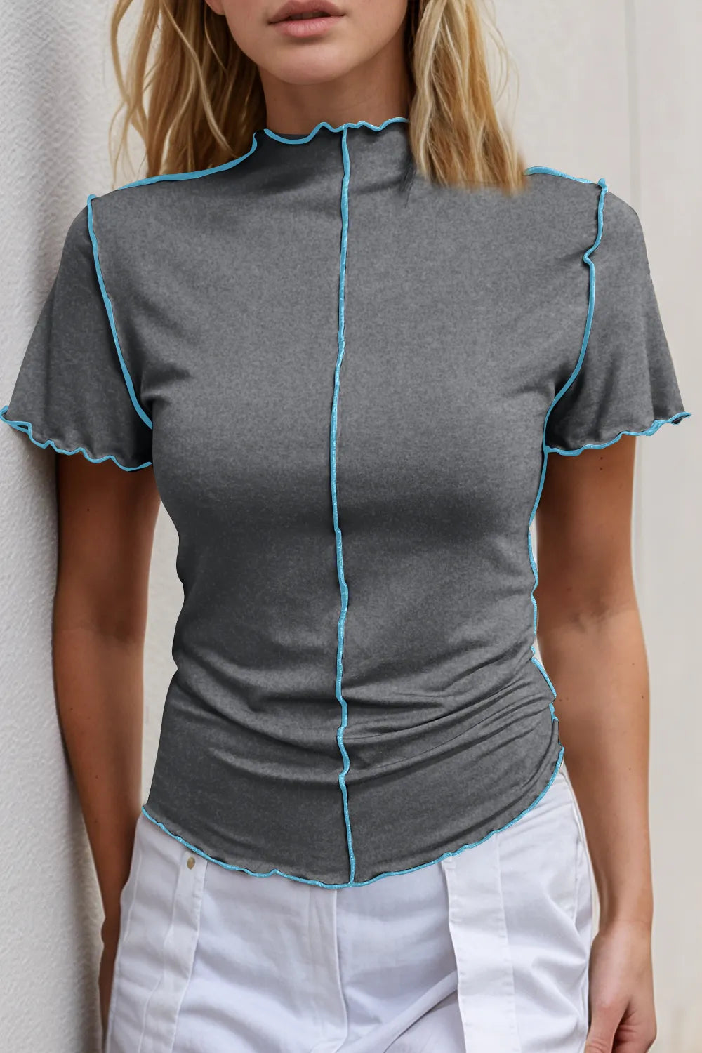 Woman wearing a gray short-sleeve top with blue trim against a neutral background