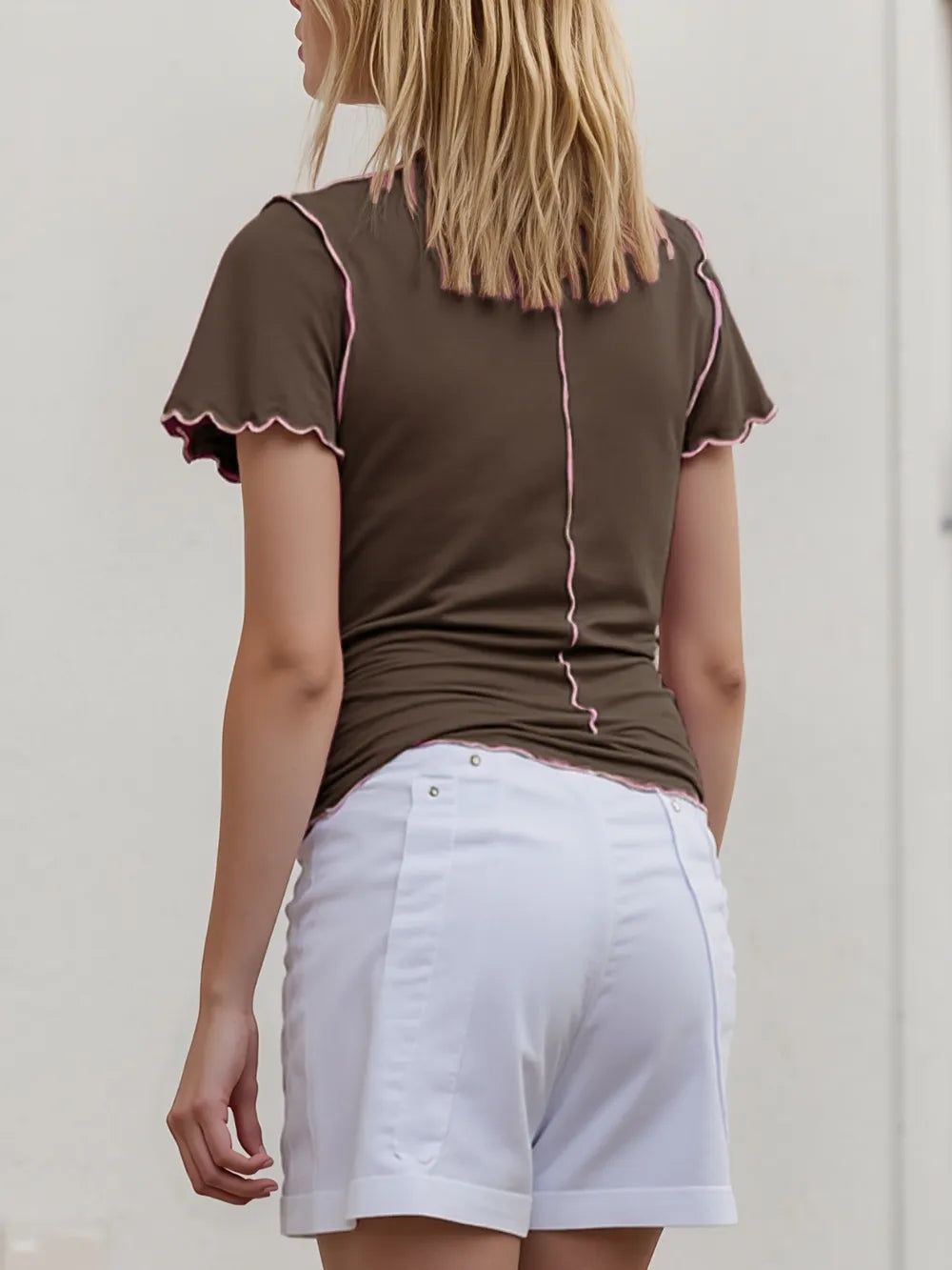 Woman wearing a brown blouse with pink trim and white shorts against a plain background