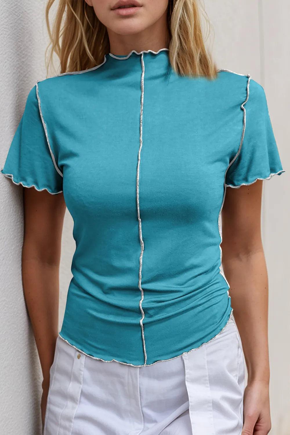 Woman wearing a teal top with white trim against a neutral background