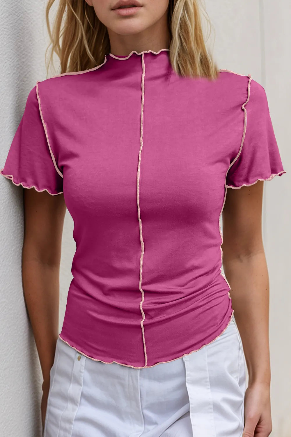 Woman wearing a pink top with ruffled trim against a neutral background