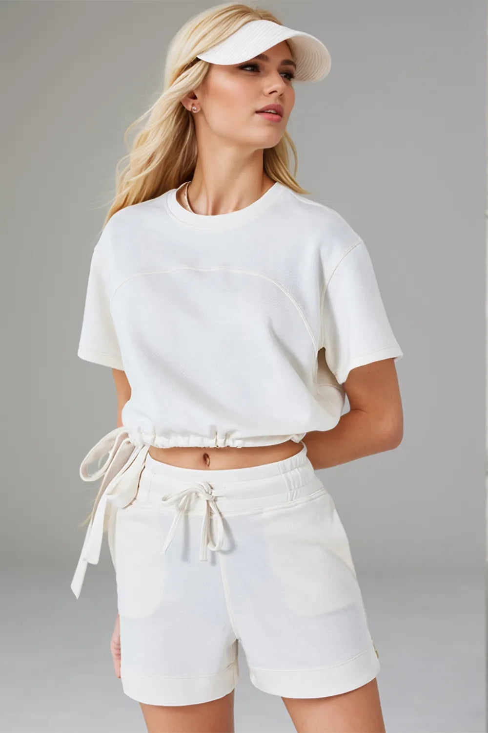 Woman wearing a white outfit with shorts and a crop top against a gray background