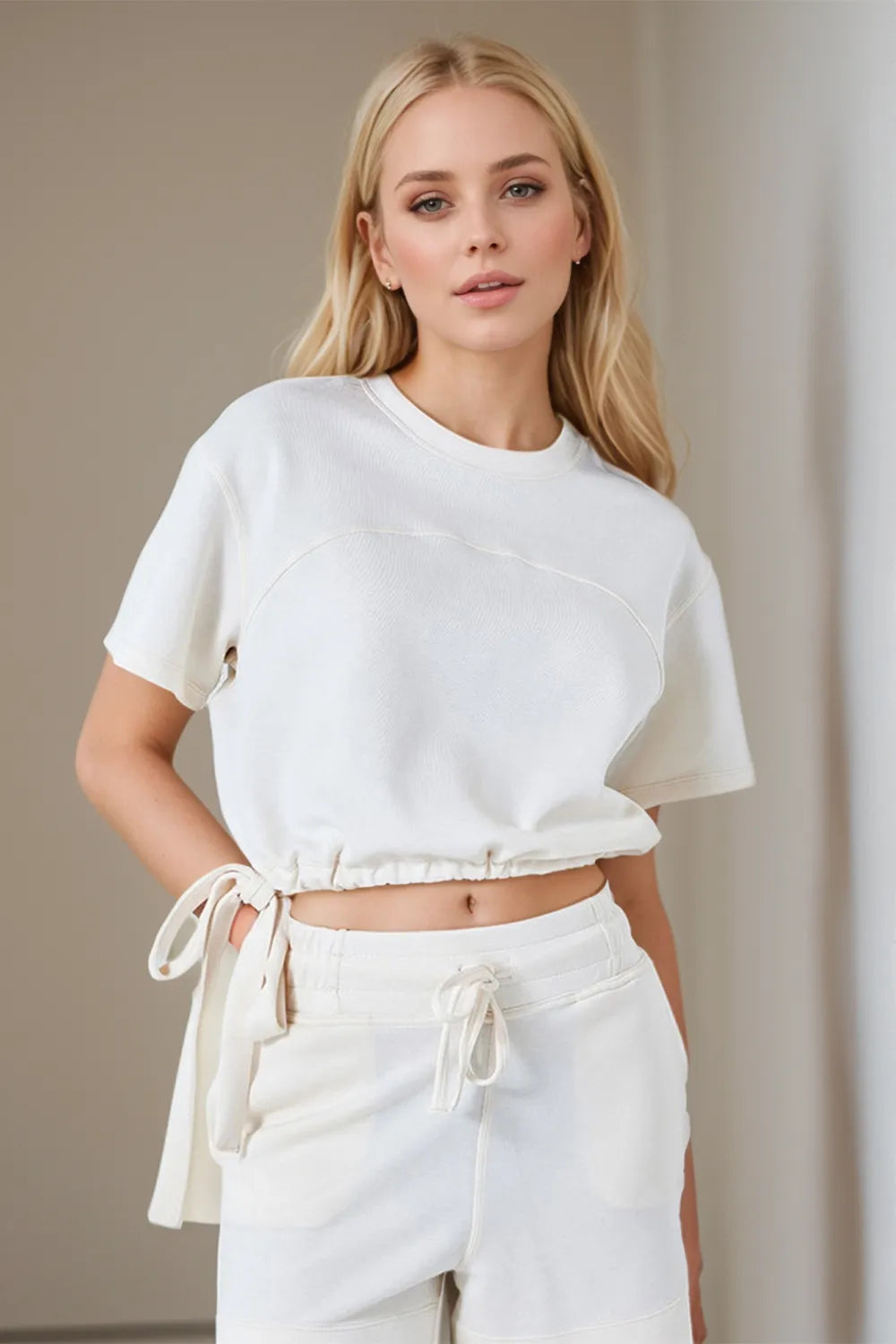 Woman wearing a white crop top and pants against a neutral background