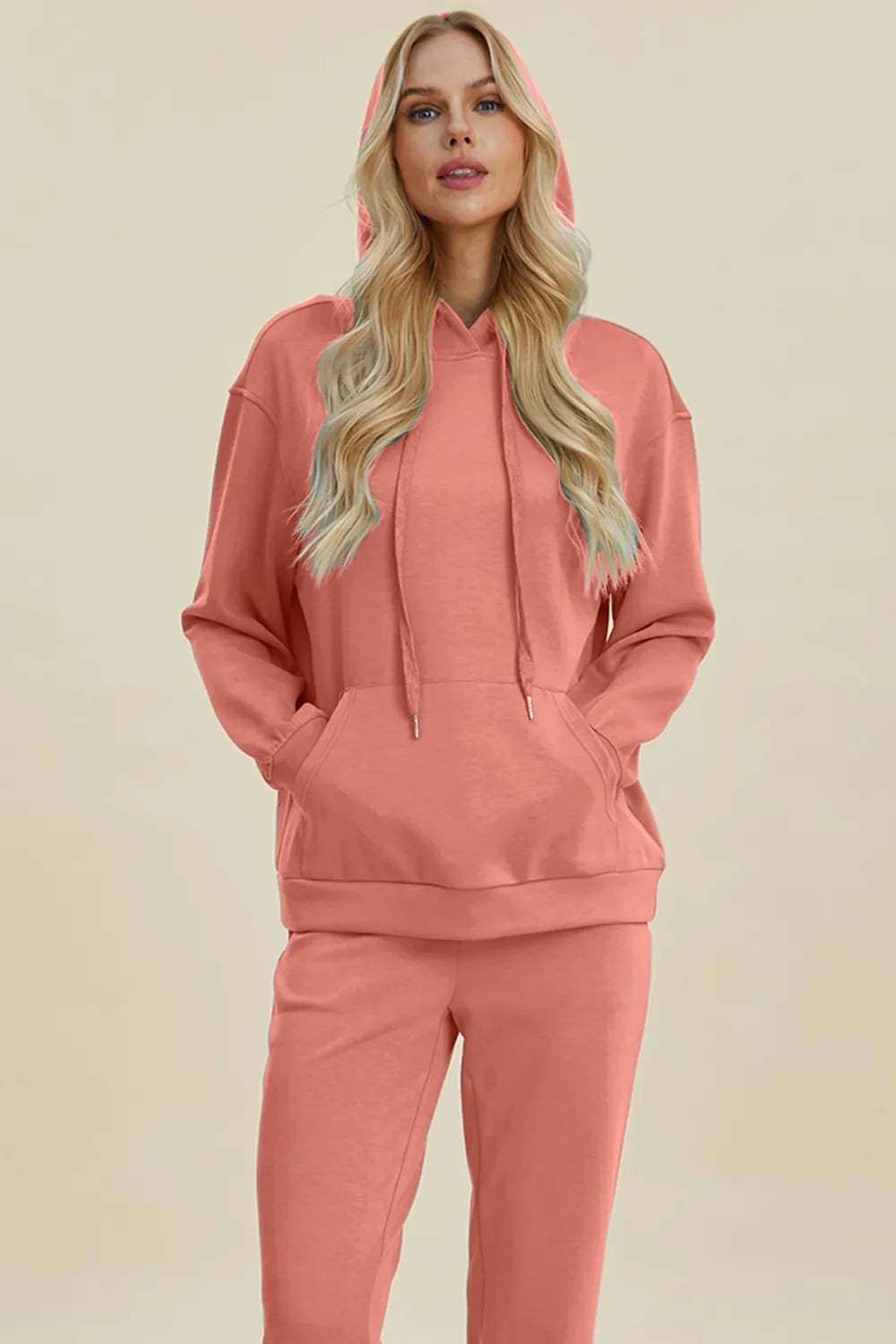 Woman wearing a pink hoodie and pants set on a beige background