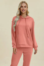 Woman wearing a coral pink hoodie and pants on a beige background