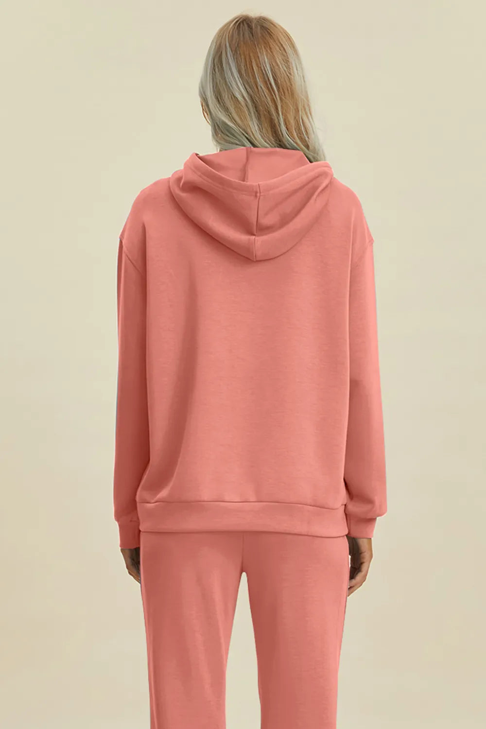 Person wearing a pink hoodie and pants on a beige background