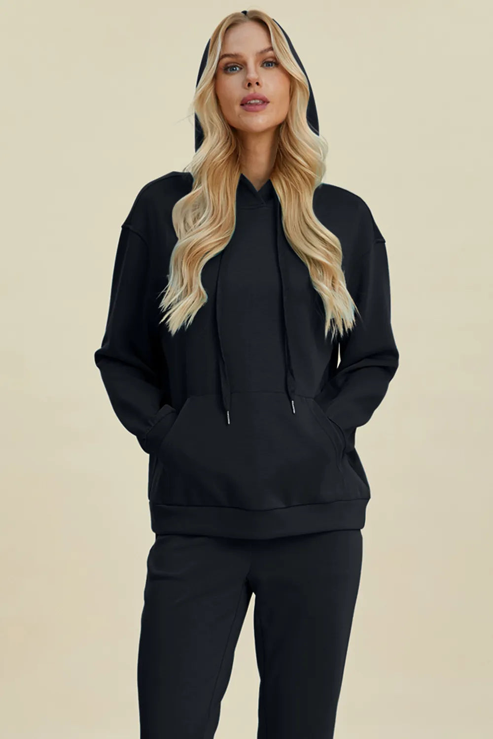 Woman wearing a black hoodie and pants on a beige background