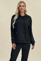 Woman wearing a black hoodie and pants on a beige background
